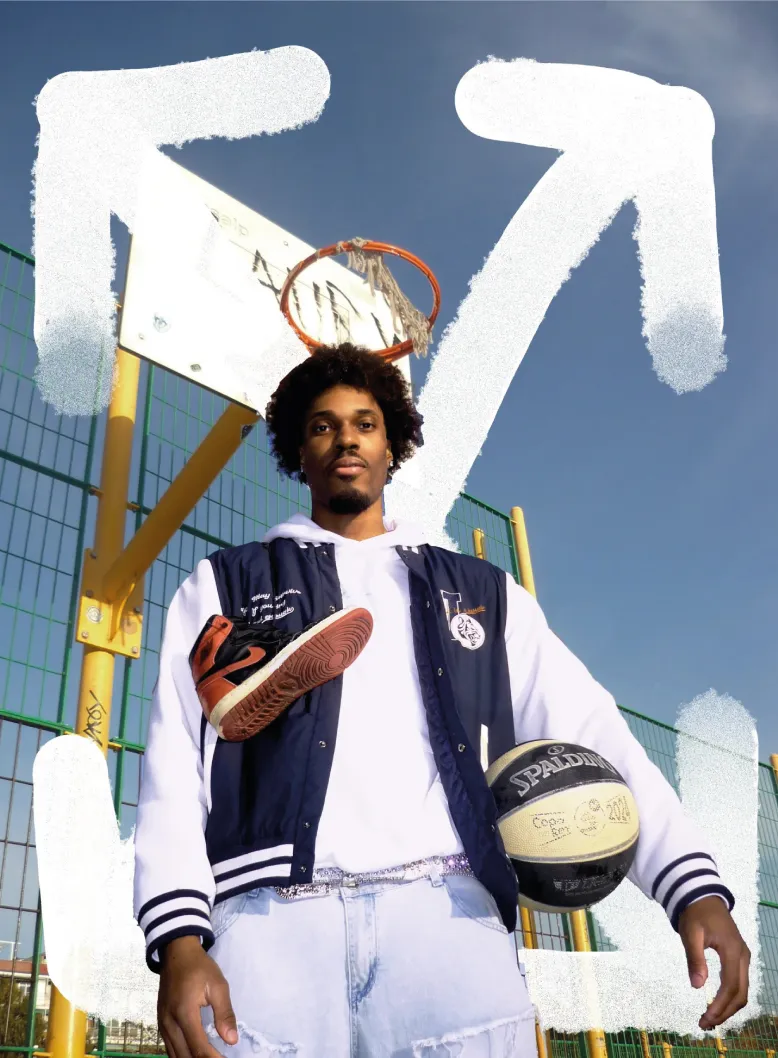 Man holding basketball and shoe on outdoor court.