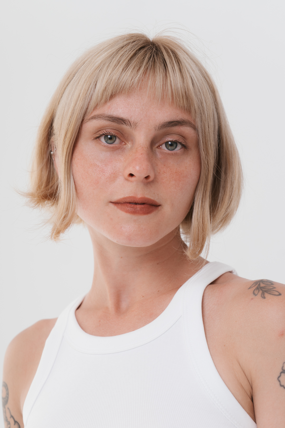 Woman with short blonde hair, wearing white tank top.