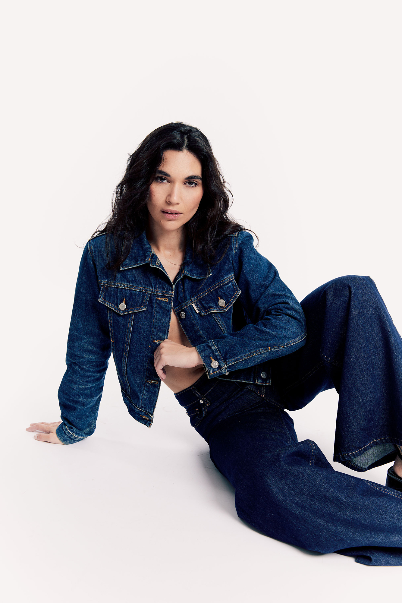 Woman in denim jacket and jeans sitting pose.