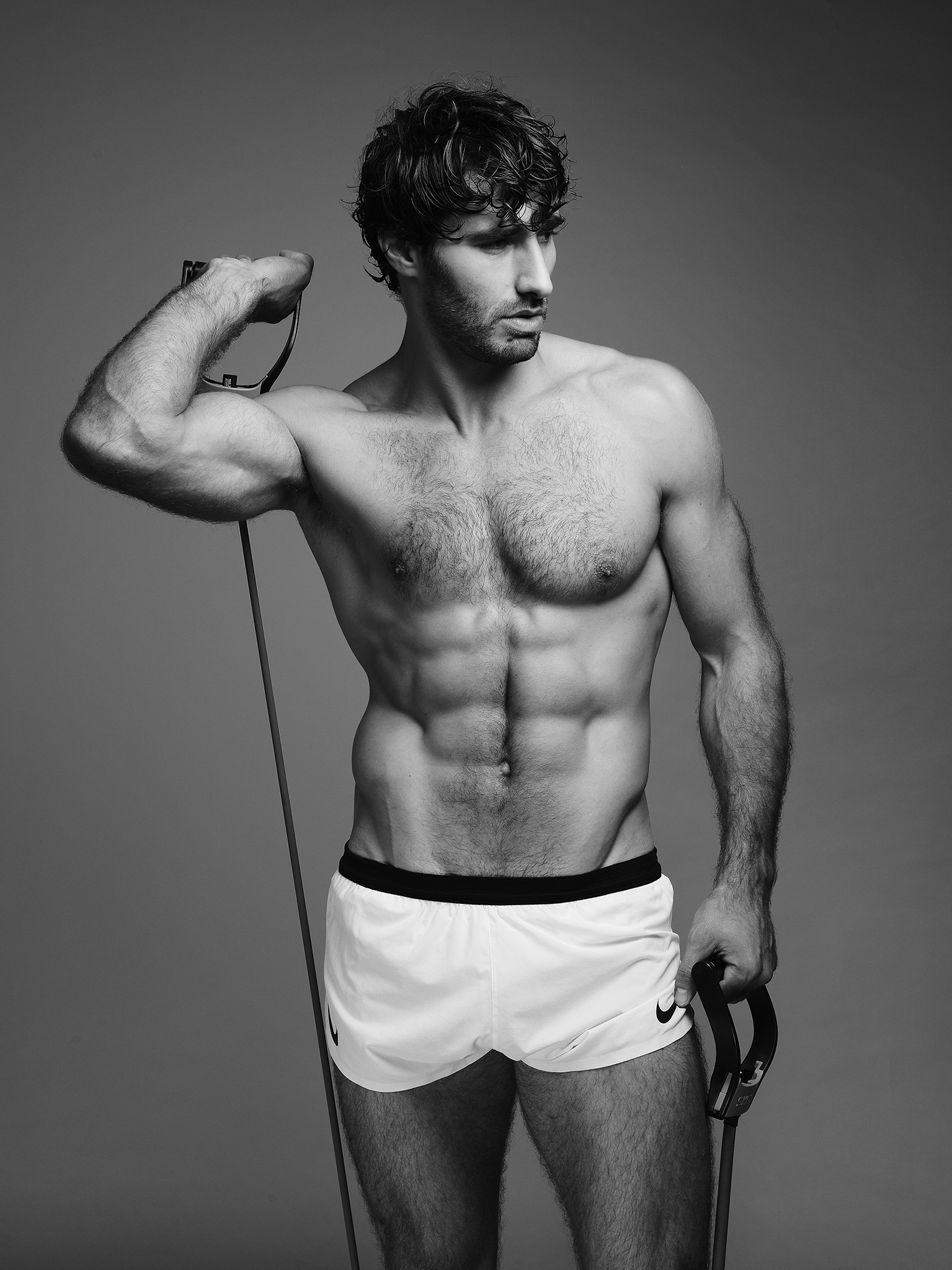 Man exercises with resistance bands, wearing white shorts.