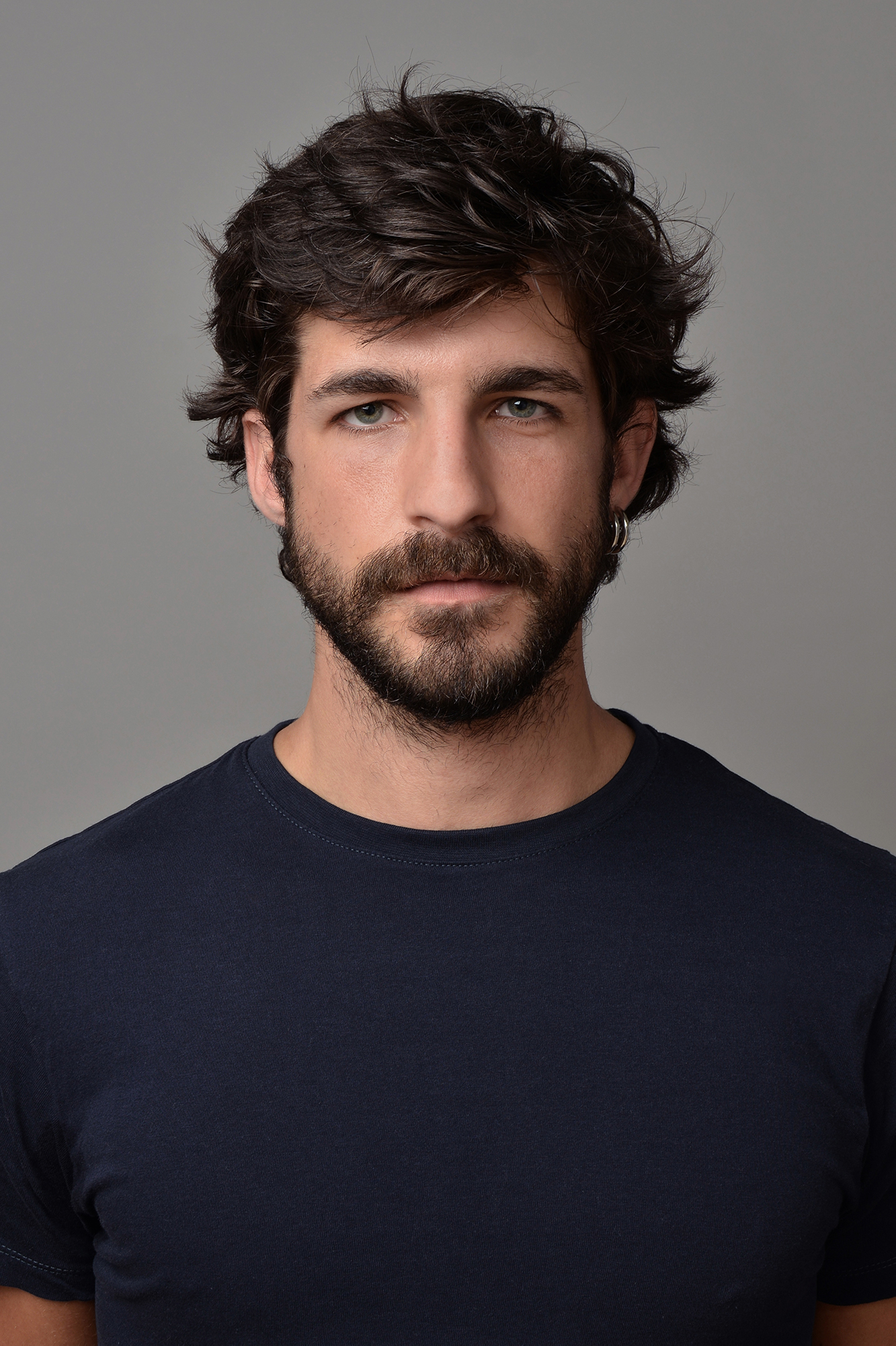 Man with beard in dark shirt, neutral background.