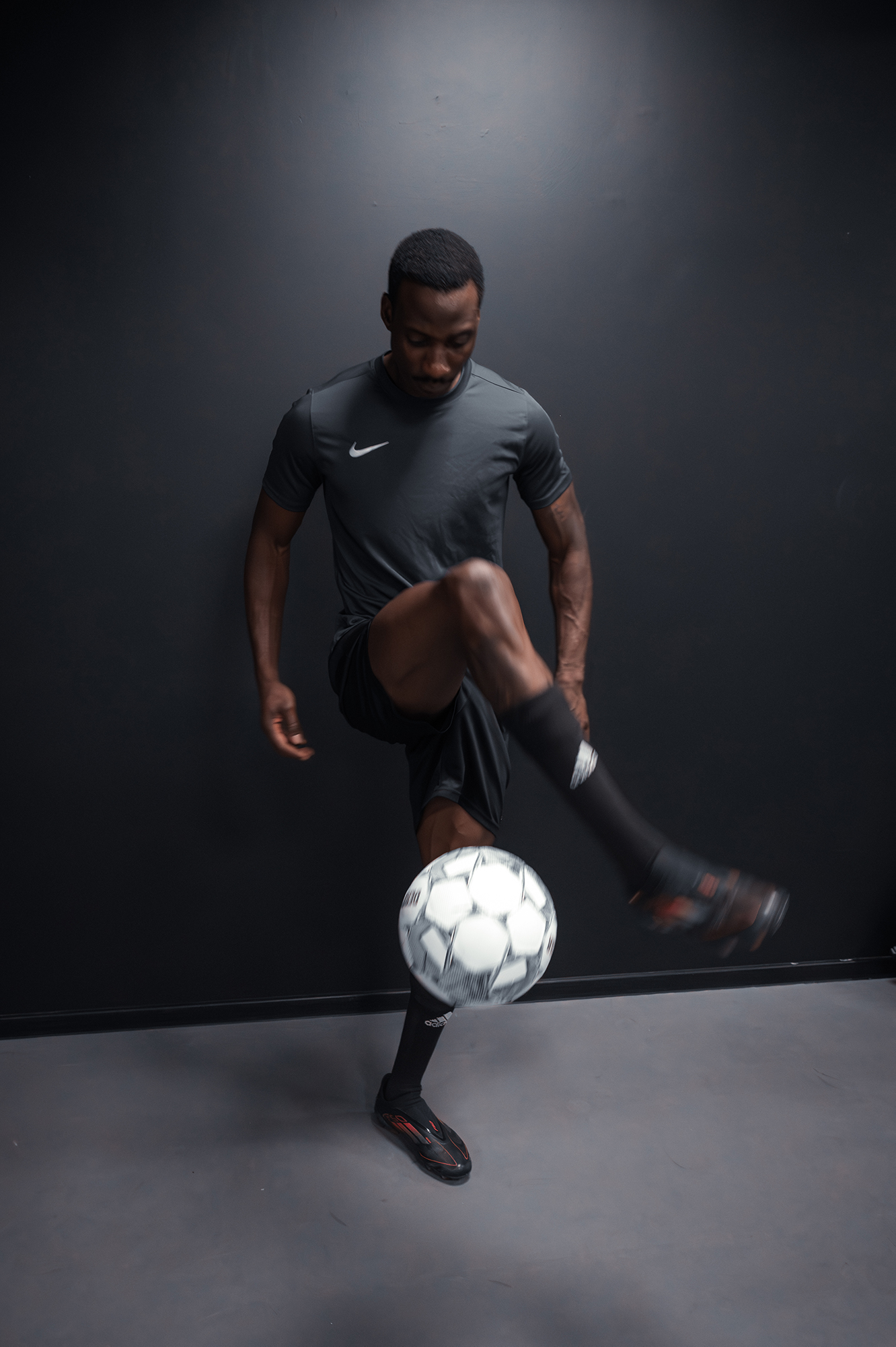 Man practicing soccer indoors with black uniform.