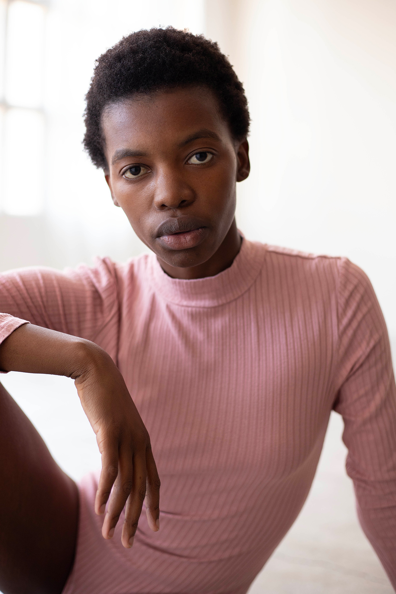 Person wearing pink ribbed turtleneck shirt looking thoughtful.