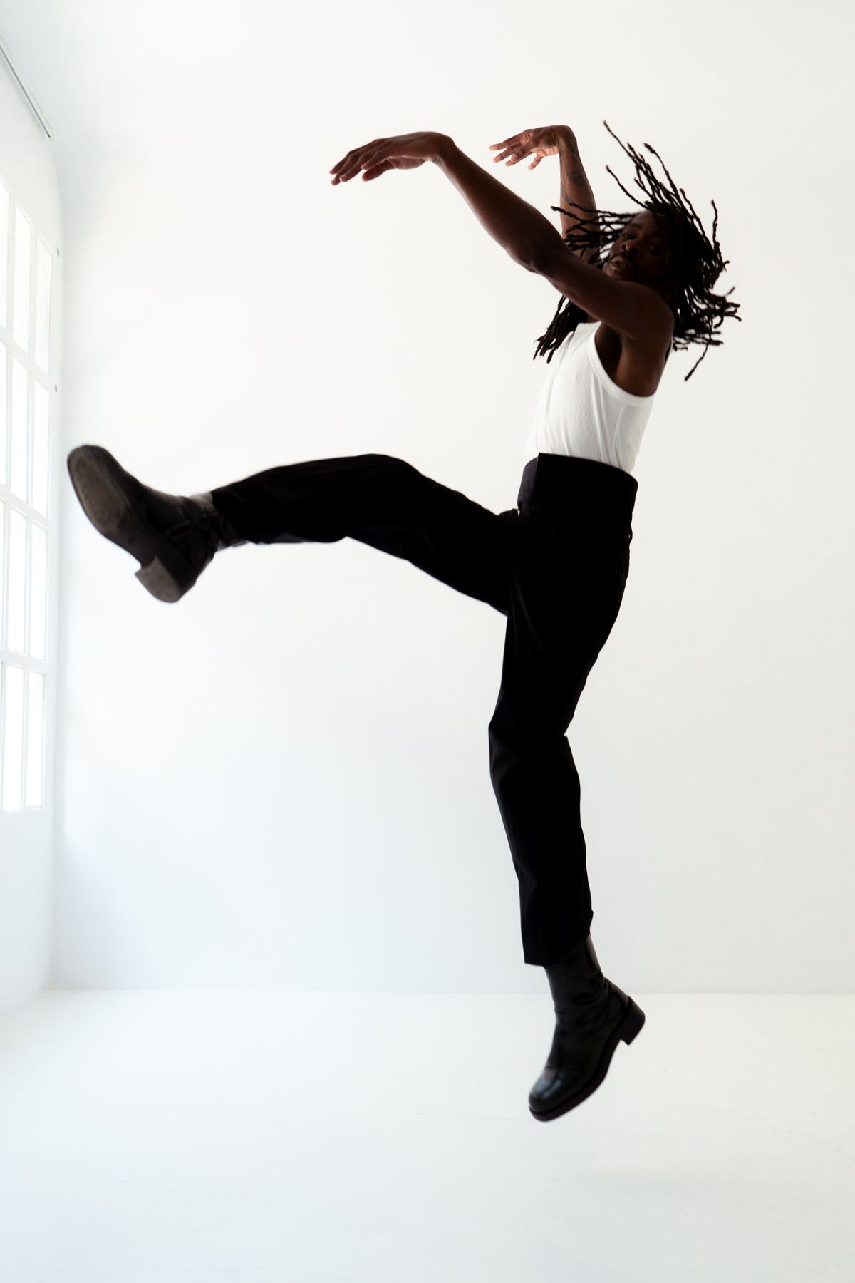 Person leaping with outstretched arms, black pants, white top.