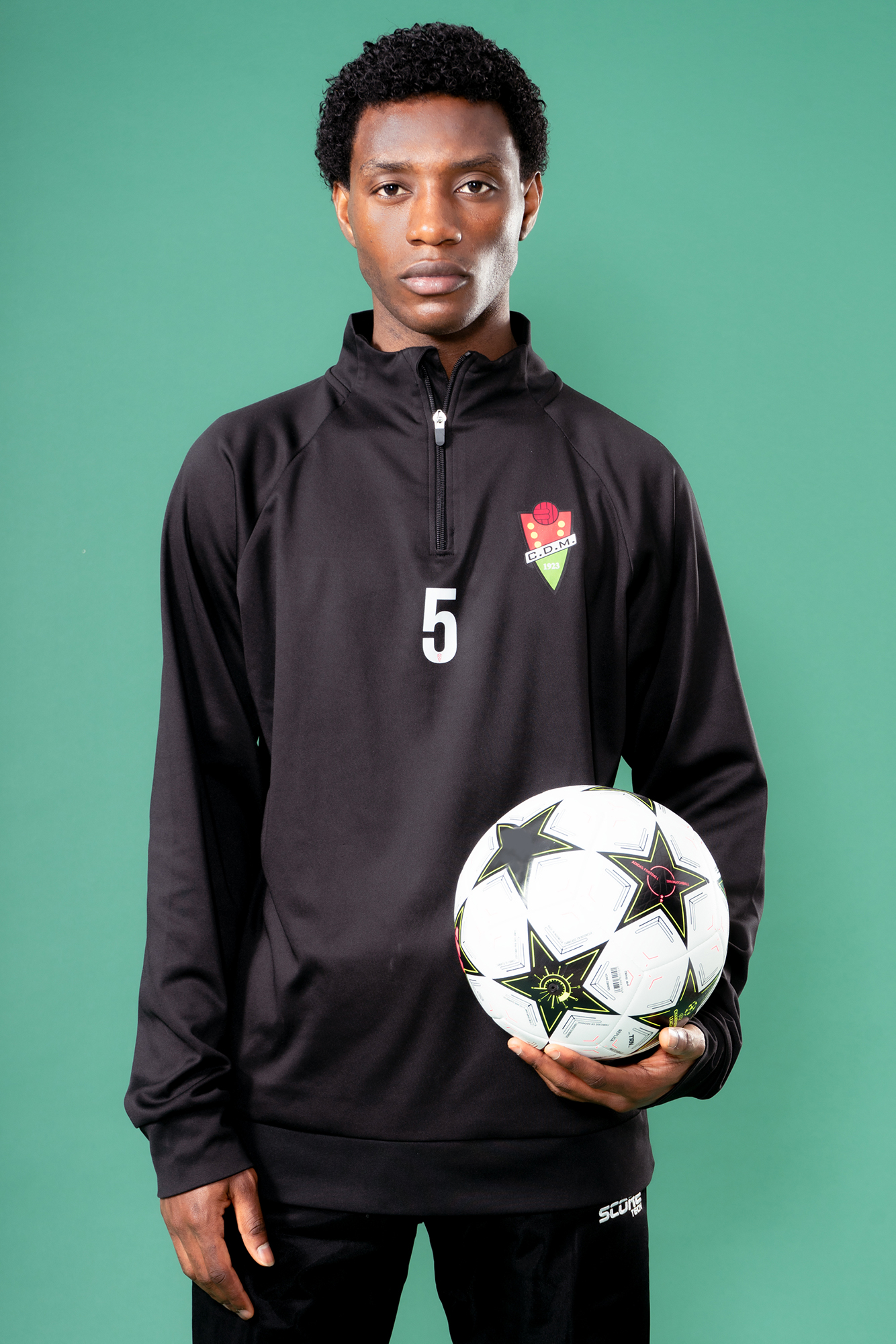 Soccer player holding ball, wearing team jacket.