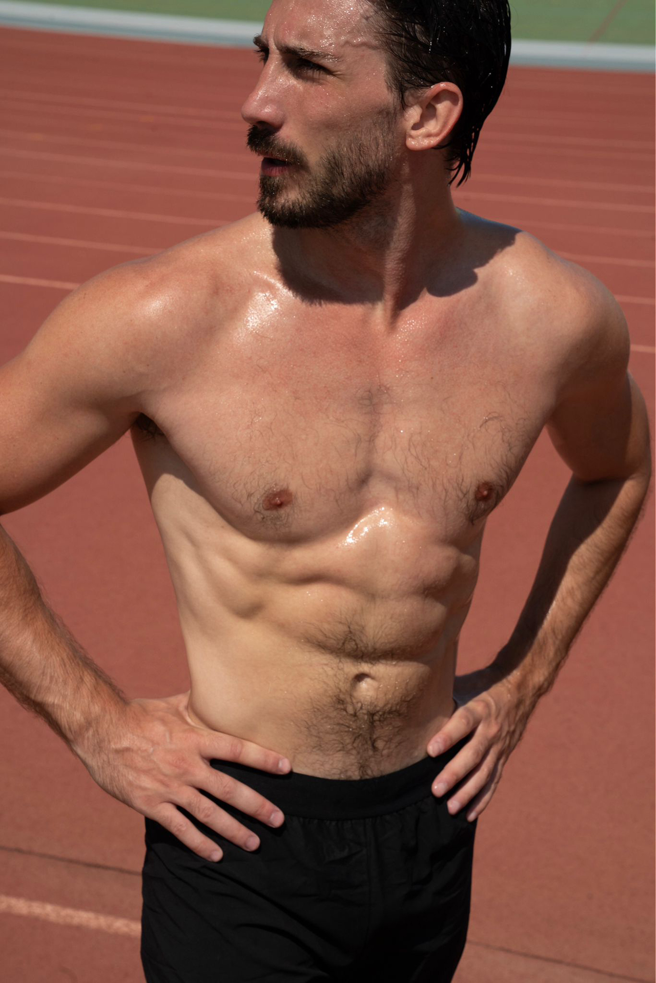 Shirtless athlete on track sweating after workout.