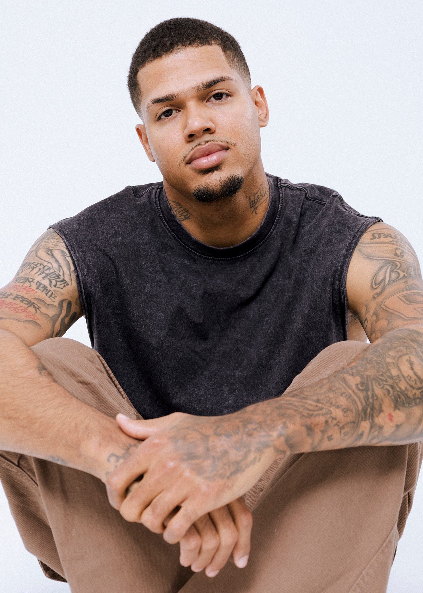 Man with tattoos sitting against white background.
