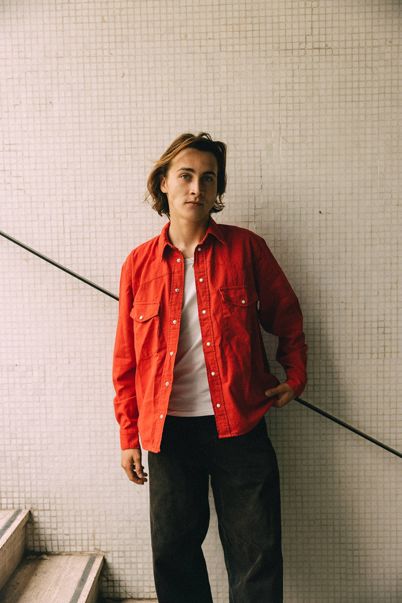 Person in red shirt leaning against a tiled wall.