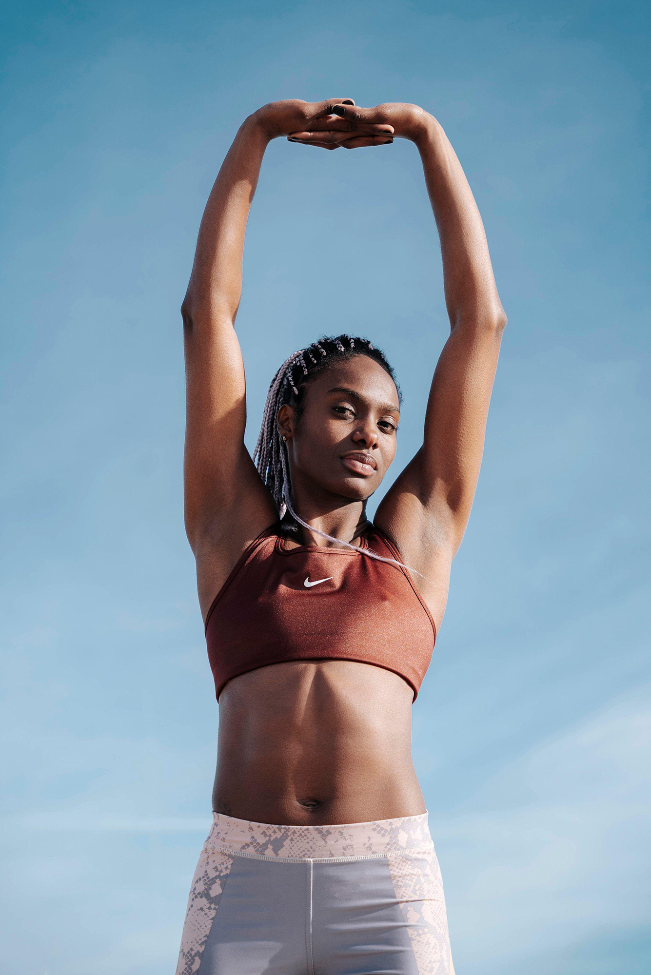 Woman stretching arms outdoors, clear blue sky backdrop.