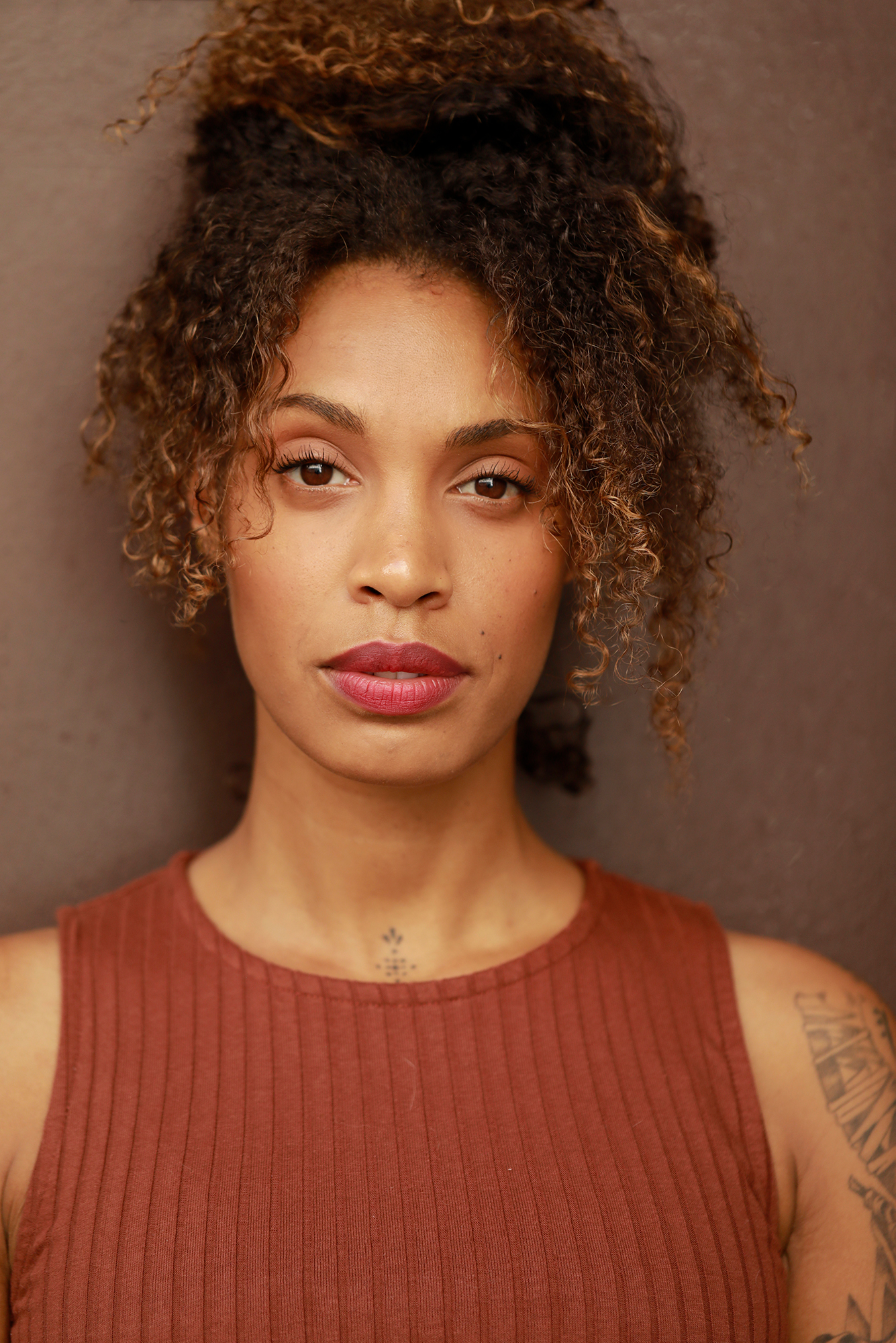 Person with curly hair, wearing brown top.