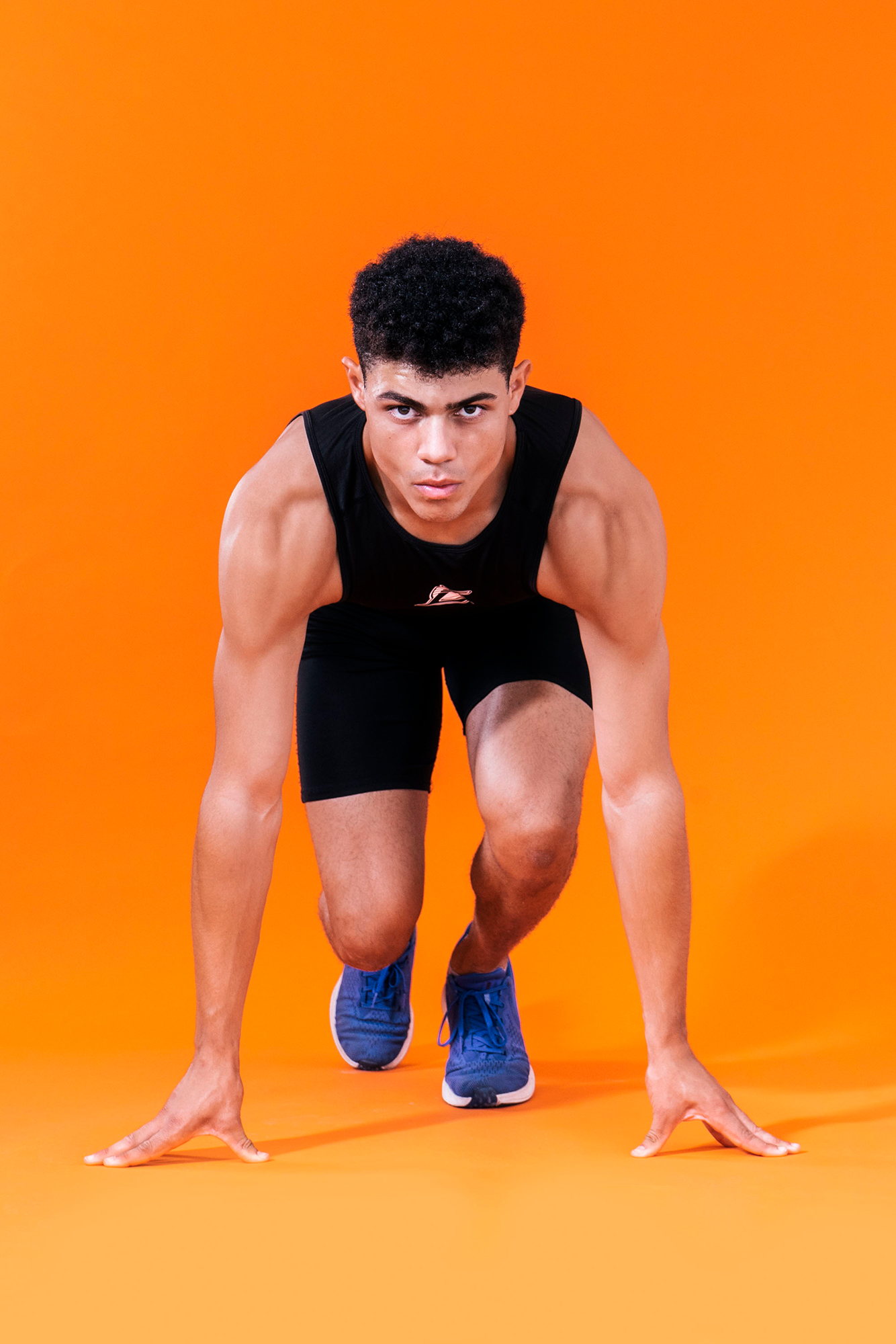 Athlete preparing to sprint on orange background.